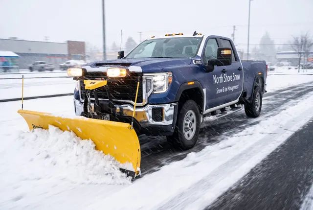 North Shore Snow plow truck pushing snow across a commercial parking lot during a snowfall