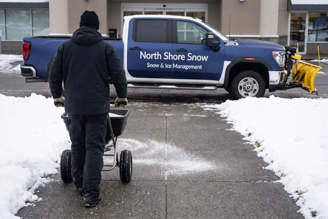 North Shore Snow crew member pushing a walk-behind spreader along a cleared commercial walkway